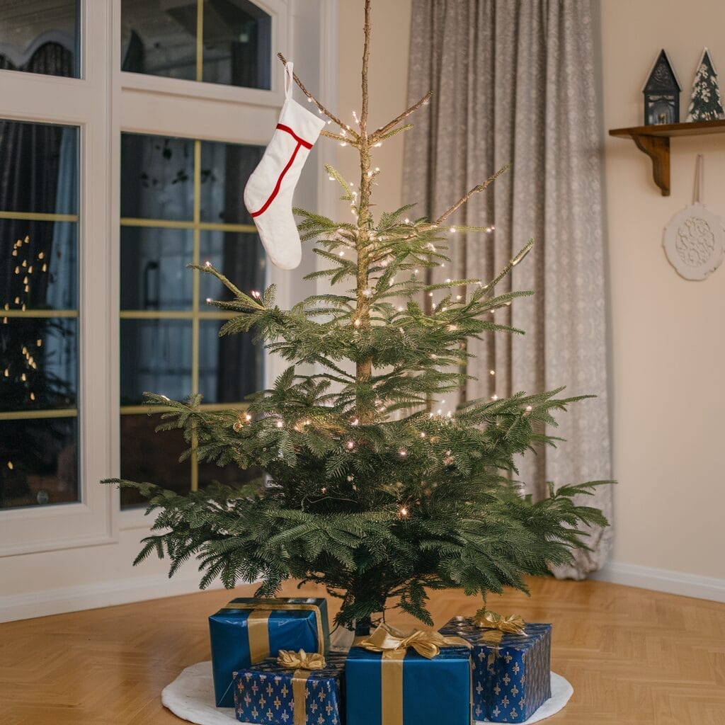 Minimalist Christmas tree with lights, a single stocking, and three blue gift boxes with gold ribbons on a wooden floor by a window.